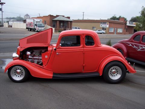 1972 Ford Ranchero - A bright red hot rod coupe is parked on the street with its hood open, revealing the engine.