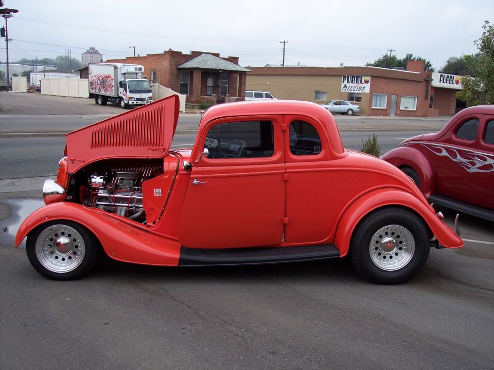 red hot rod coupe with hood open, another red car with flames in background