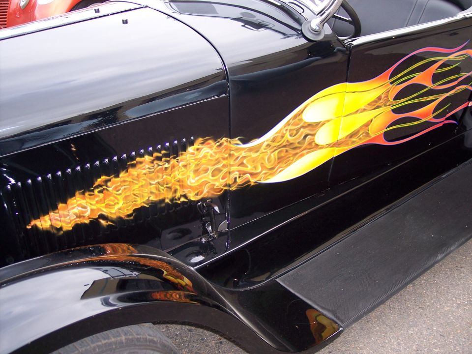 Black hot rod car side view with yellow and orange flame graphics on the fender and door