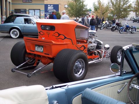 1972 Ford Ranchero - A custom hot rod pickup truck with flame decals and oversized rear tires is parked next to other vehicles and motorcycles.