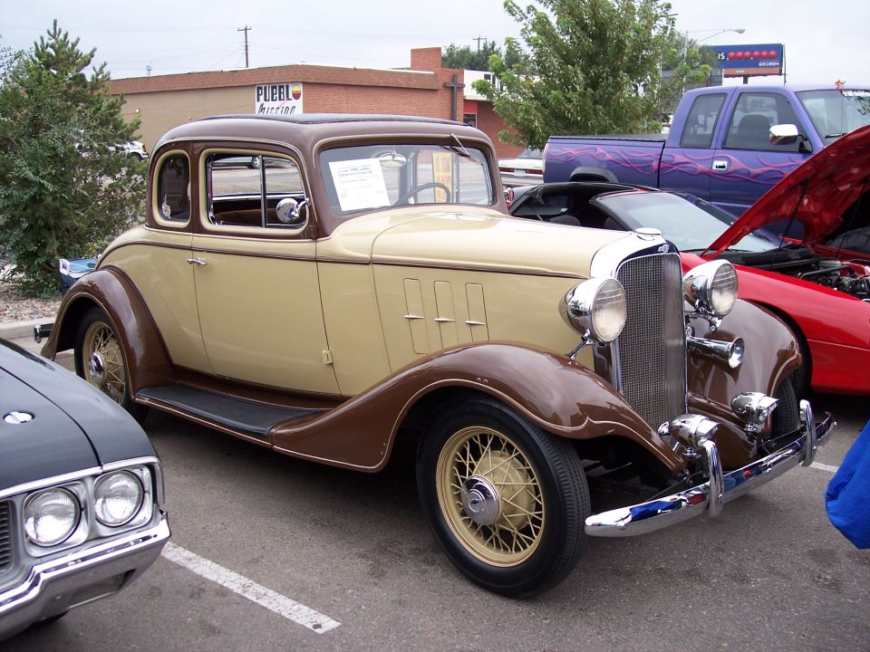 Two-tone brown and tan coupe with wire wheels parked next to a black car