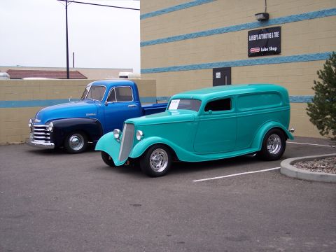 1972 Ford Ranchero - Two vintage vehicles, a teal panel van and a blue pickup truck, are parked in front of a building.