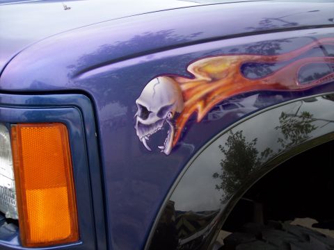 1972 Ford Ranchero - Airbrushed skull and flames adorn the fender of a purple vehicle, with an orange turn signal in view.