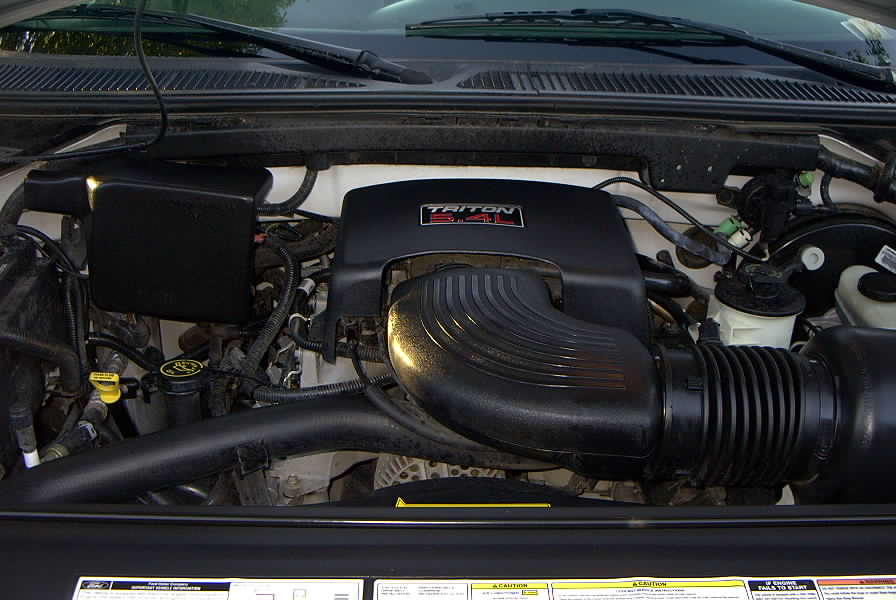 Ford truck engine bay with black 'Triton 5.4L' intake cover and coolant reservoir