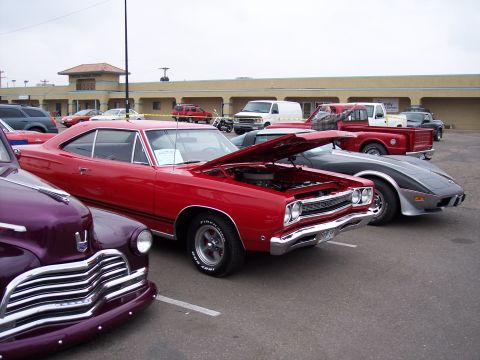 1972 Ford Ranchero - Several classic cars are parked in a lot, including a red muscle car with its hood up.