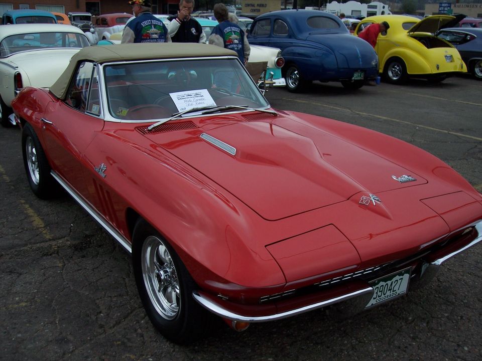 Red 1965 Corvette convertible with tan top, front 3/4 view. License plate reads 390427