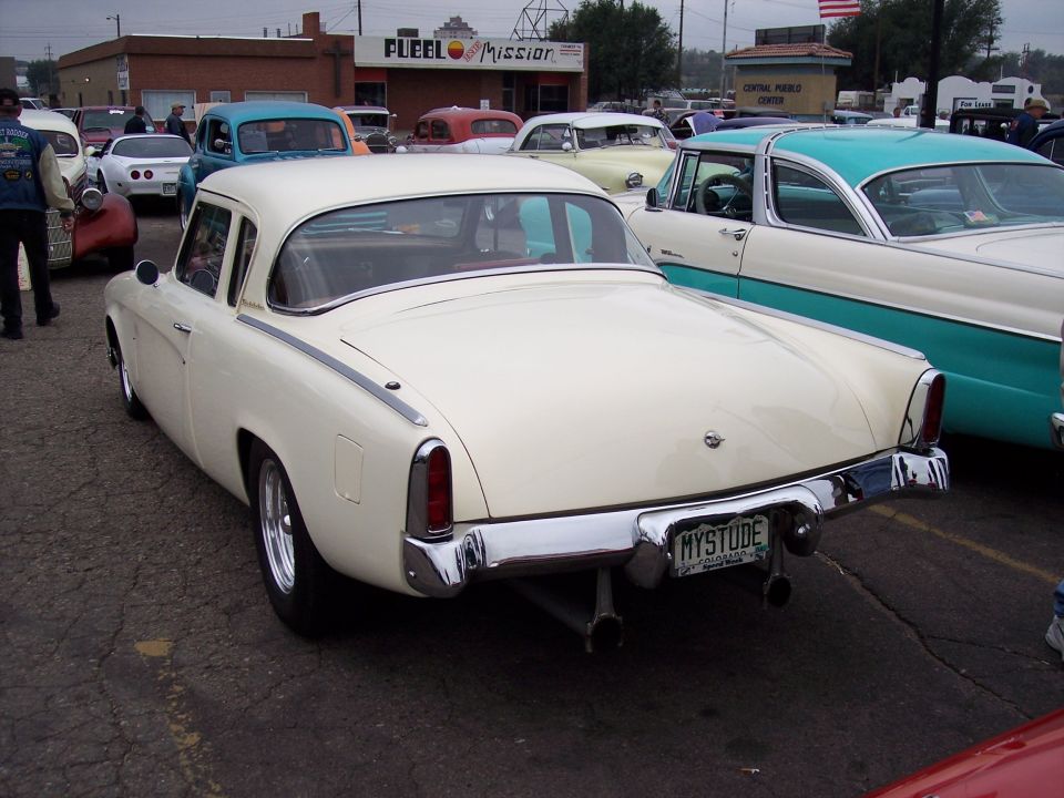1955 Studebaker coupe with custom exhaust and 'MYSTUDE' license plate, parked at a car show