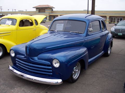 1972 Ford Ranchero - A shiny blue 1941 Ford coupe is parked next to a yellow coupe, with a modern SUV in the background.