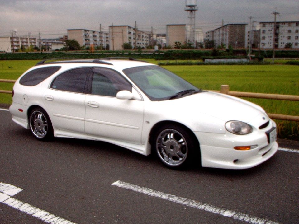 White Ford Taurus wagon with body kit and chrome wheels parked by a field in Japan