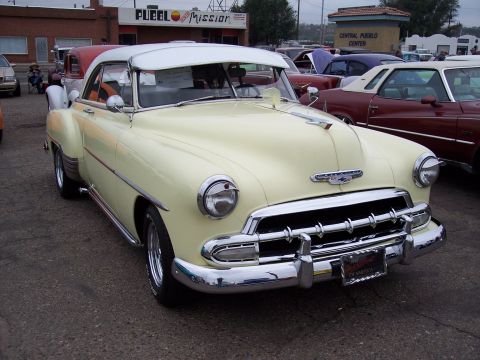 1972 Ford Ranchero - A yellow 1950 Chevrolet coupe with a white roof is parked at a car show, with other vehicles visible in the background.