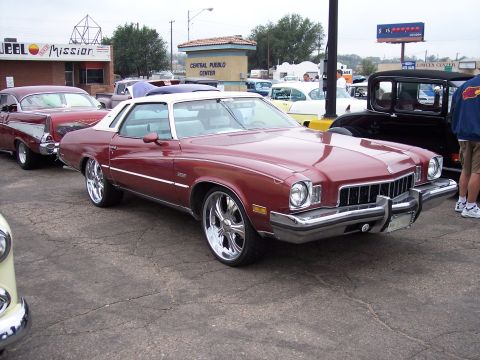 1972 Ford Ranchero - Maroon 1975 Buick Century with chrome wheels and white vinyl roof parked at a car show.
