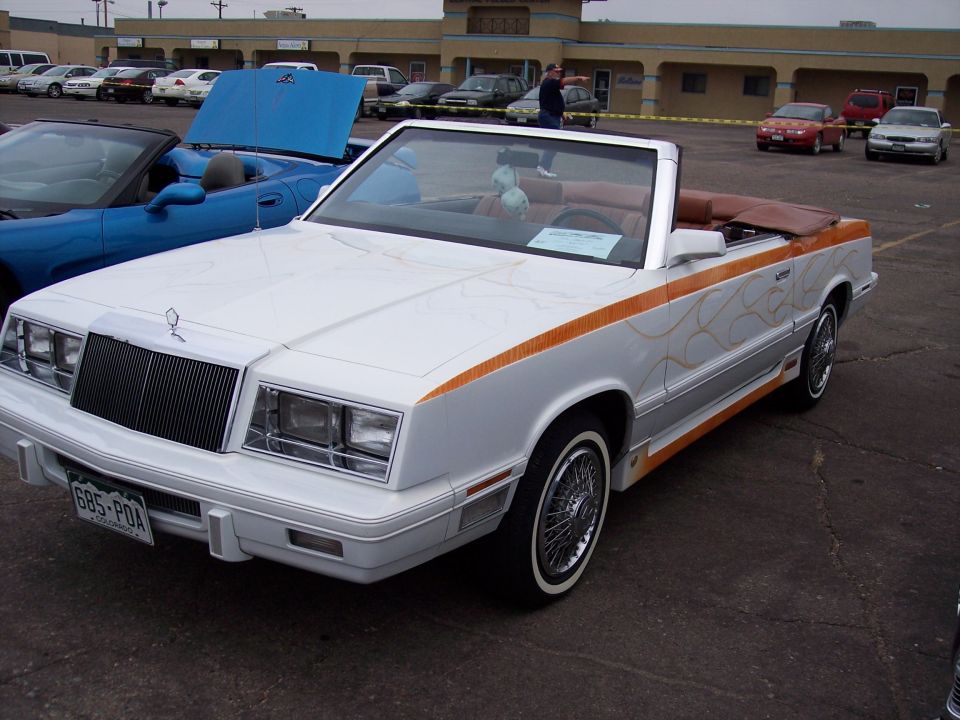 White convertible with orange flame graphics and wire wheels. A blue convertible is parked next to it