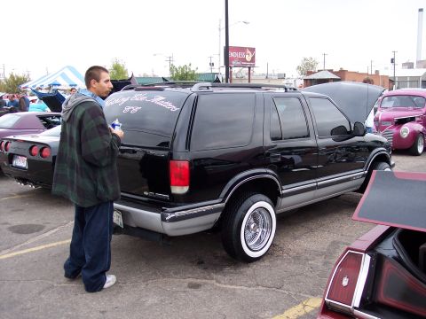 1972 Ford Ranchero - A man stands by a black SUV with custom wheels at a car show.