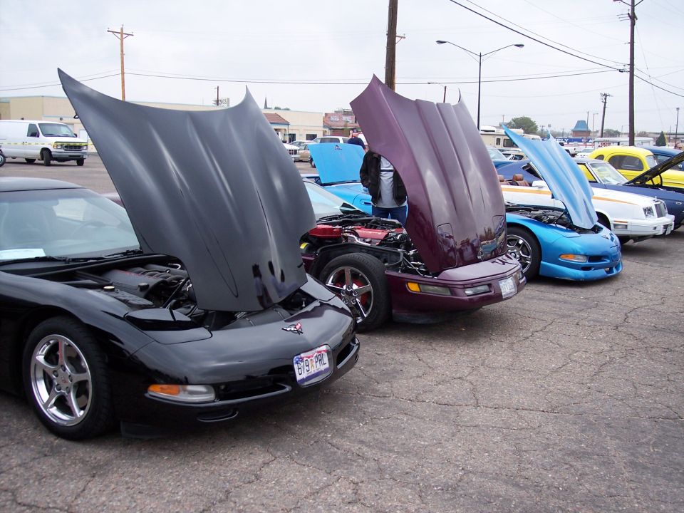 Several Corvettes parked in a row with hoods open, showing engines