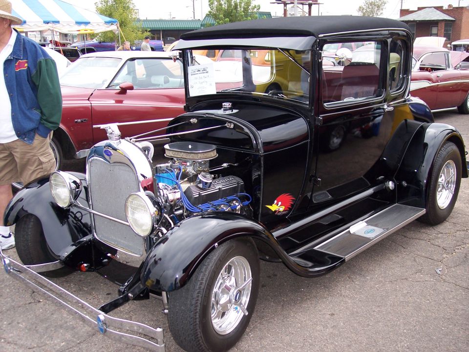 Black hot rod coupe, likely 1930s model, with Woody Woodpecker decal on fender. Other cars visible in background