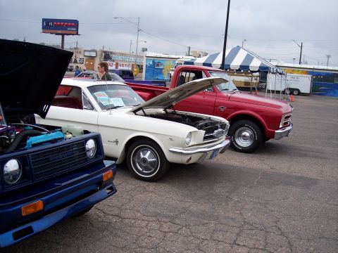 1972 Ford Ranchero - A white 1965 Ford Mustang and a red pickup truck are displayed at an outdoor event with their hoods open.