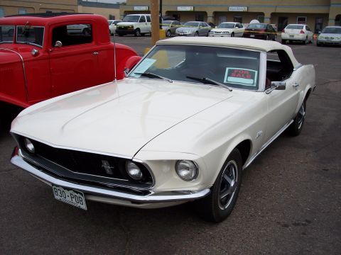 1972 Ford Ranchero - White 1969 Ford Mustang convertible parked next to a red coupe, with other cars in background.