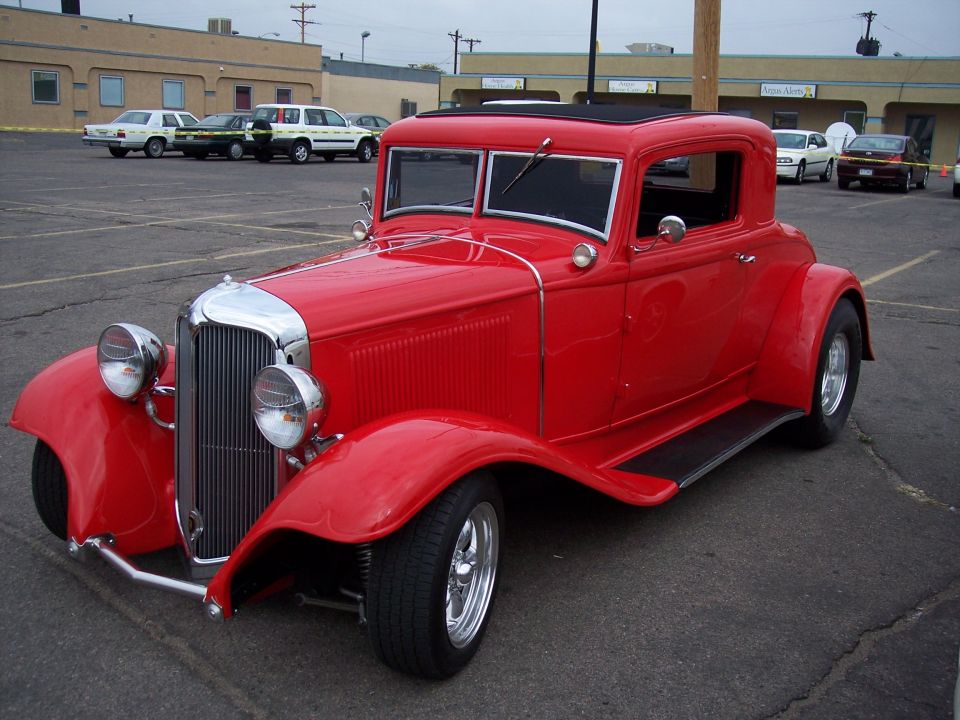 red coupe hot rod with chrome grille and headlights, parked in a lot