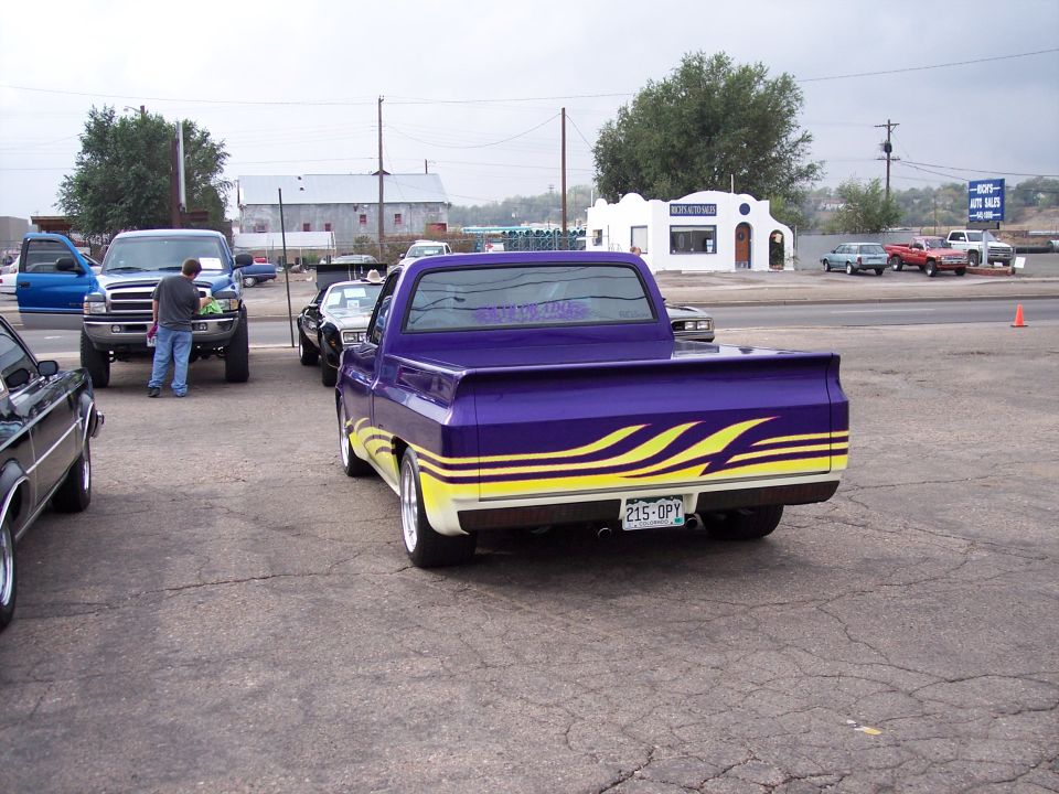 Purple pickup truck with yellow flame graphics on the side and a spoiler. Other vehicles are parked nearby