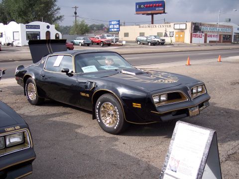 1972 Ford Ranchero - Black 1977 Pontiac Trans Am parked outside with other vehicles and businesses in background.