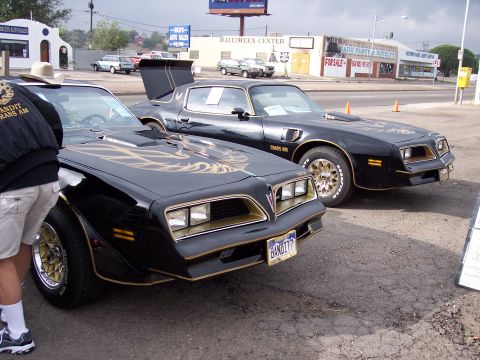 1972 Ford Ranchero - Two black Pontiac Firebirds, likely Trans Ams, are parked side-by-side with gold accents and decals visible.