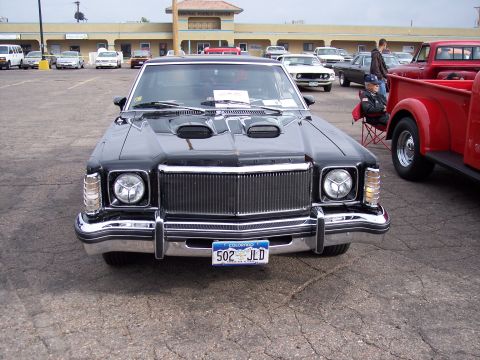 1972 Ford Ranchero - A black 1972 Ford Ranchero is parked in a lot with other vehicles and a building in the background.