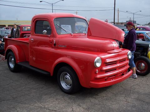 1972 Ford Ranchero - A bright red Dodge pickup truck is displayed with its hood open at a car show, alongside other vehicles.