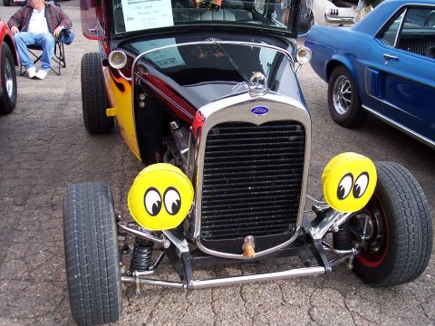 1972 Ford Ranchero - A modified hot rod with custom yellow headlights sits parked next to a blue car.