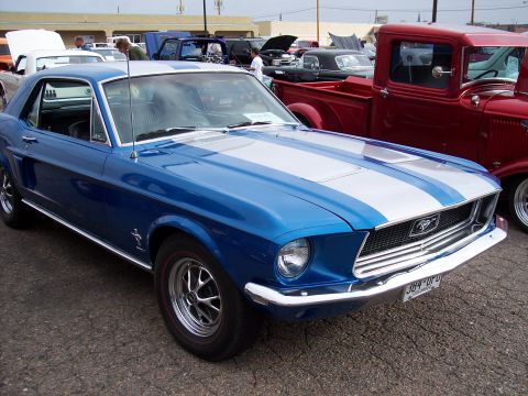 1972 Ford Ranchero - A blue 1967 Ford Mustang fastback with silver racing stripes is parked at an outdoor car show.