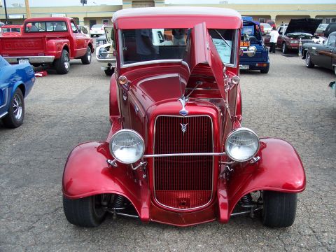 1972 Ford Ranchero - A shiny red vintage Ford pickup truck is displayed with its hood up, surrounded by other vehicles at an outdoor event.