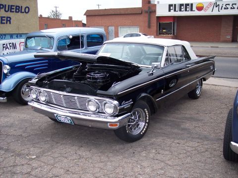 1972 Ford Ranchero - A black convertible with its hood open is parked next to a blue vintage car, with a building in the background.