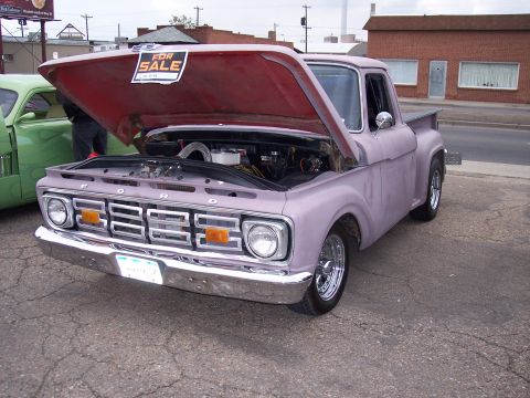 1972 Ford Ranchero - A purple 1965 Ford pickup truck is parked with its hood open, displaying a 'For Sale' sign, next to a green car.