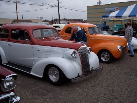 1972 Ford Ranchero - A red and white sedan and an orange coupe are displayed at a car show under a cloudy sky.