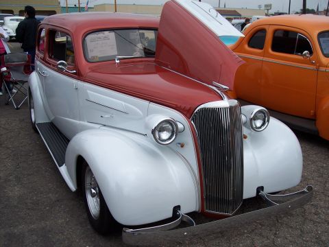 1972 Ford Ranchero - A two-tone red and white sedan is parked next to an orange car at a show.