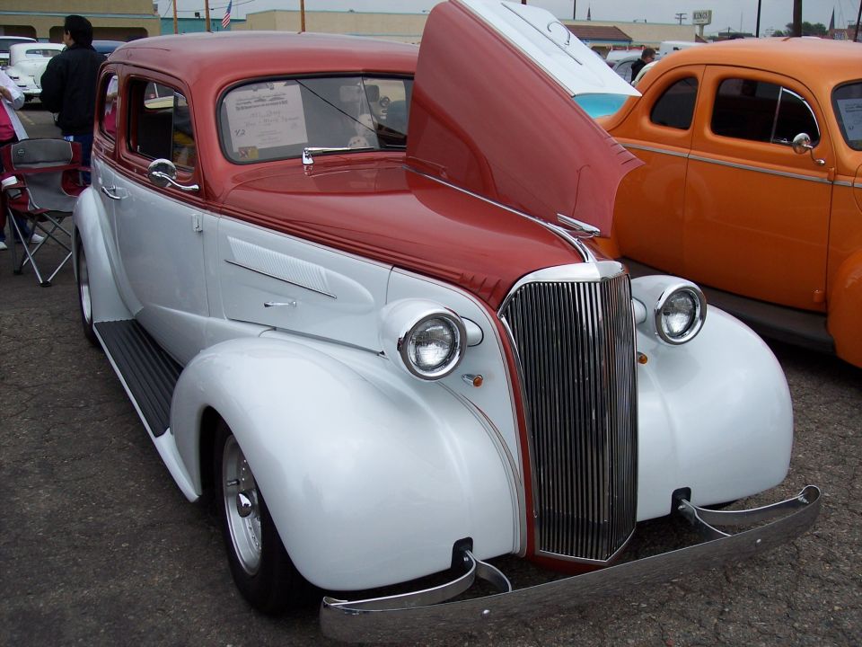 Red and white sedan with hood open, chrome grille, and bumper