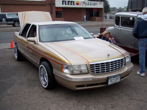 1972 Ford Ranchero - A tan Cadillac sedan with custom pinstriping is displayed with its hood up, parked next to another vehicle.