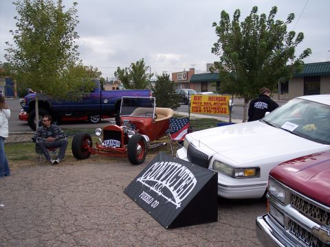 1972 Ford Ranchero - A red hot rod is displayed alongside other vehicles under an overcast sky.