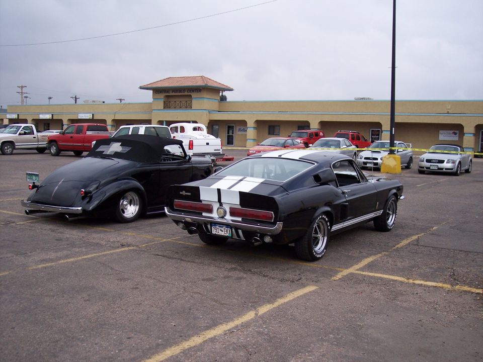 Black 1967 Ford Mustang Shelby GT500 with white stripes, parked next to a black convertible