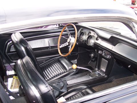1972 Ford Ranchero - The interior of a classic Ford Mustang shows its black vinyl seats, wooden steering wheel, and floor-mounted shifter.