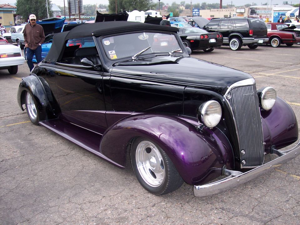 Black convertible hot rod with purple fenders and chrome grille parked at a car show