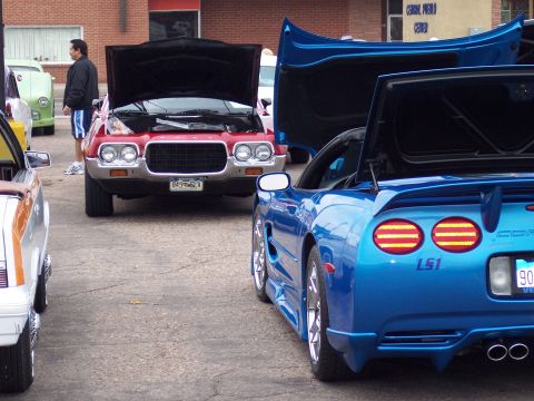1972 Ford Ranchero - A red 1972 Ford Torino GT is parked with its hood up, alongside a blue Chevrolet Corvette at an outdoor car show.
