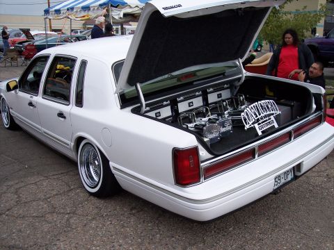 1972 Ford Ranchero - A white sedan, likely from the 1990s, displays its custom hydraulics and audio system with the trunk open.