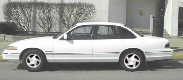 White sedan, side view, with a black trim line along the body and five-spoke wheels