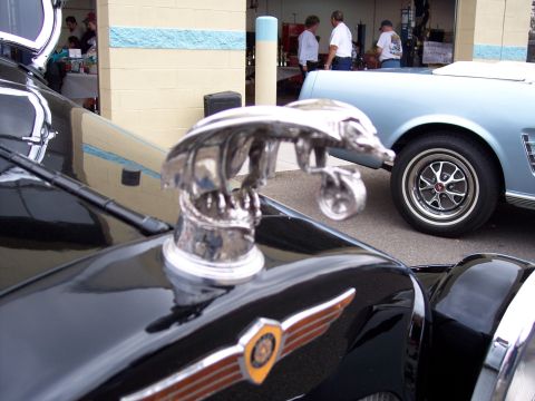 1972 Ford Ranchero - A chrome eagle hood ornament is prominent on the hood of a black classic car, with a light blue car visible behind it.