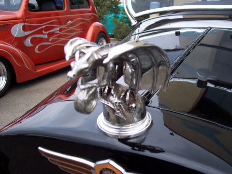 1972 Ford Ranchero - A chrome eagle hood ornament sits atop a black car, with a red hot rod visible behind it.