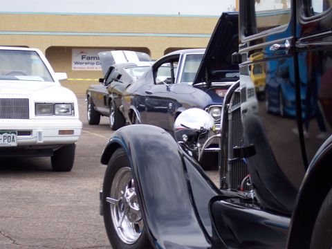 1972 Ford Ranchero - A line of cars, including a white sedan and a blue coupe, are parked in front of a building.
