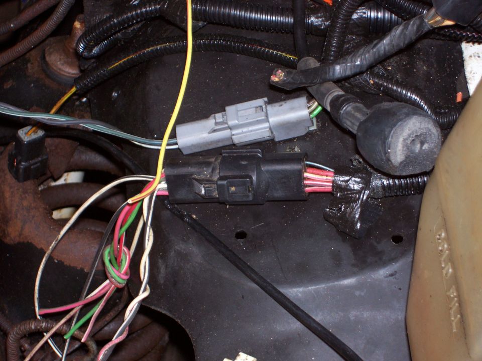 Engine bay wiring harness with two gray and black connectors, and bundled wires. Some tape is visible