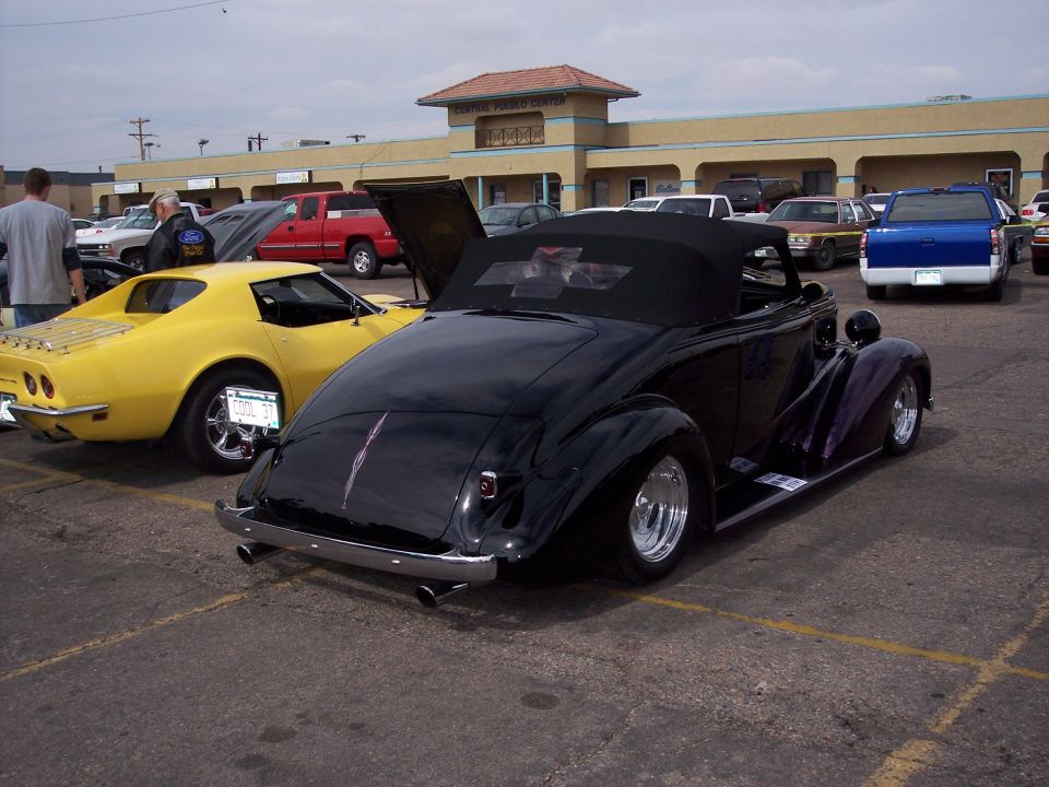 Black convertible hot rod parked next to a yellow Corvette