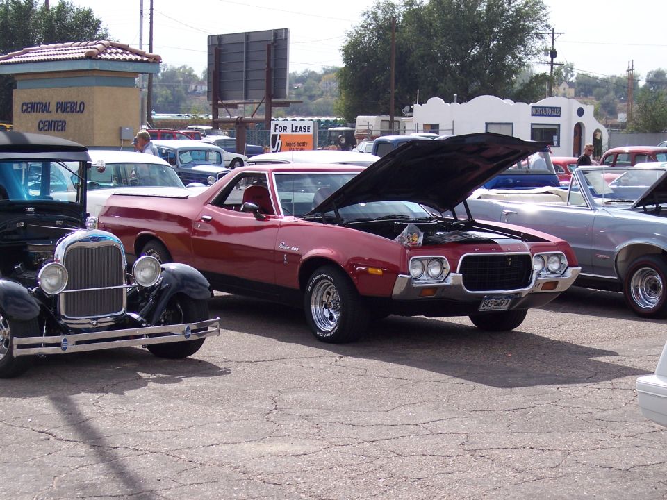 Red 1972 Ford Ranchero with hood open, parked next to a black antique car and a silver convertible
