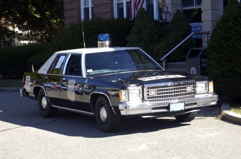 1973 Dodge 1500 - A black and white police car is parked on the street in front of a building.